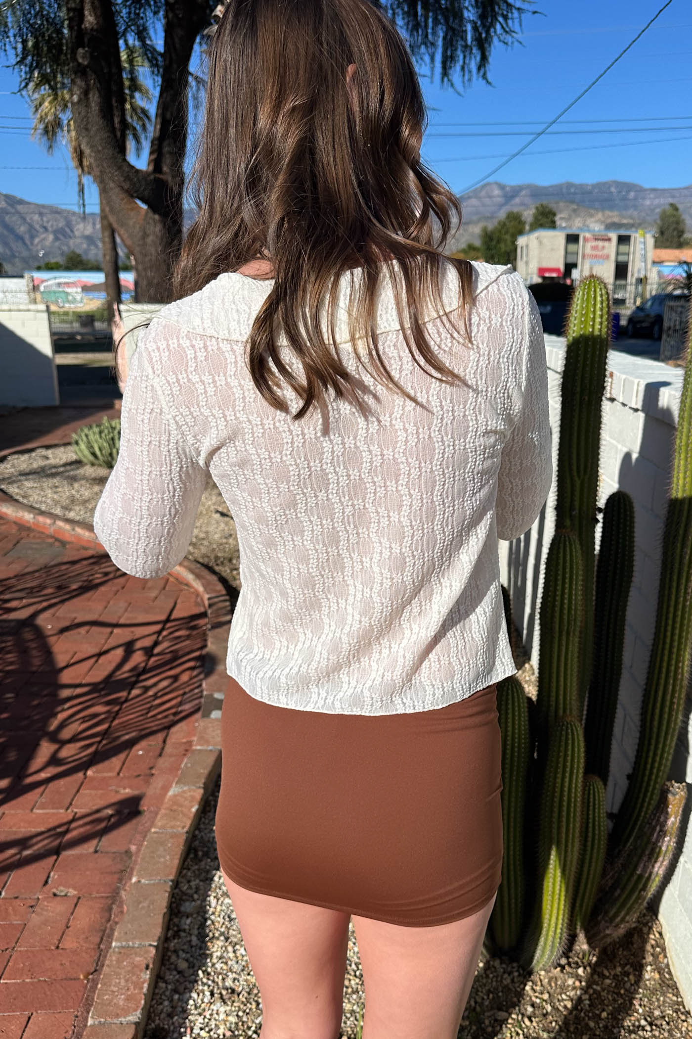 Person wearing a white top and brown shorts standing in front of cacti.