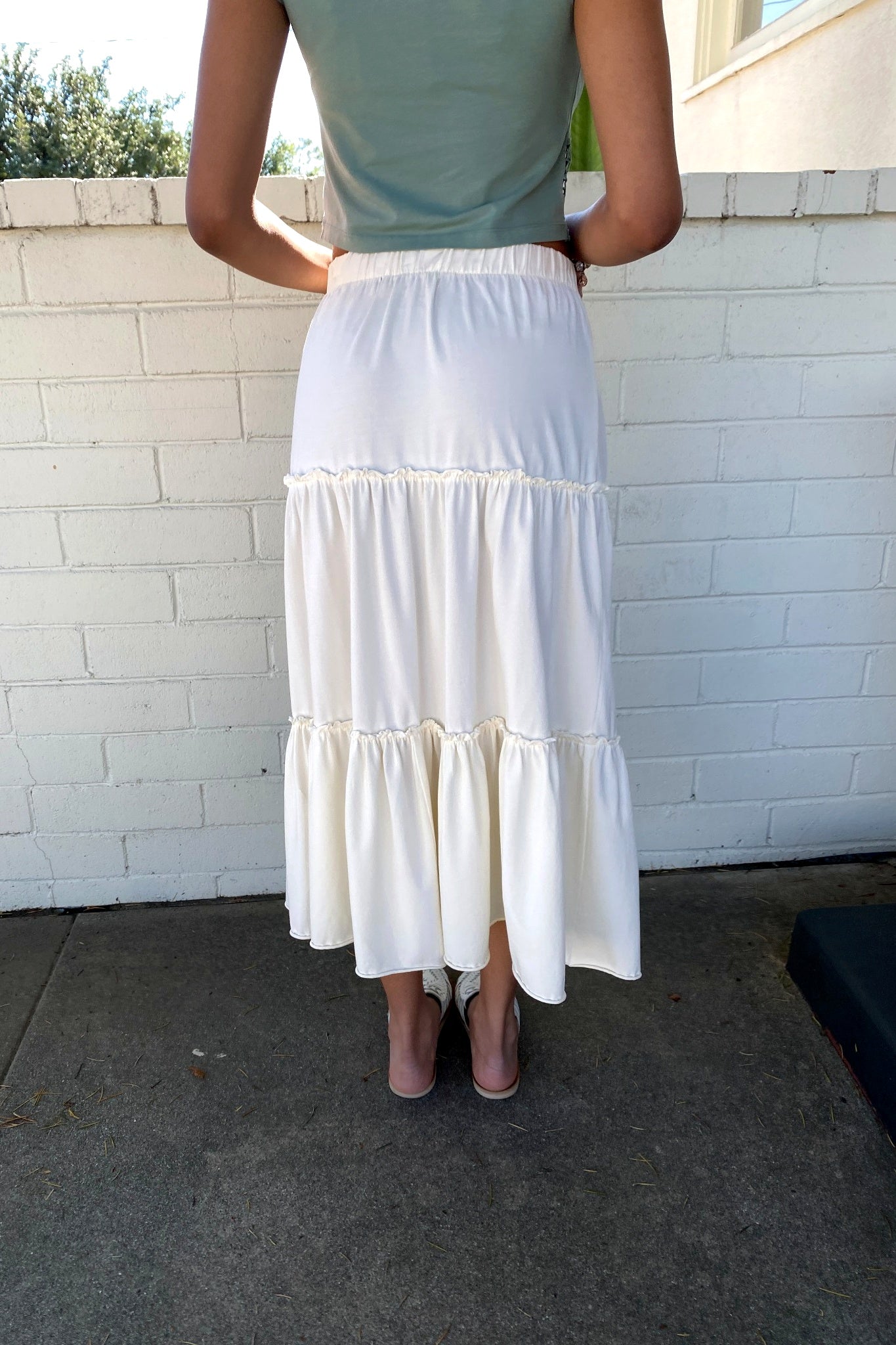 Person wearing a white tiered skirt with a light green top against a white brick wall.