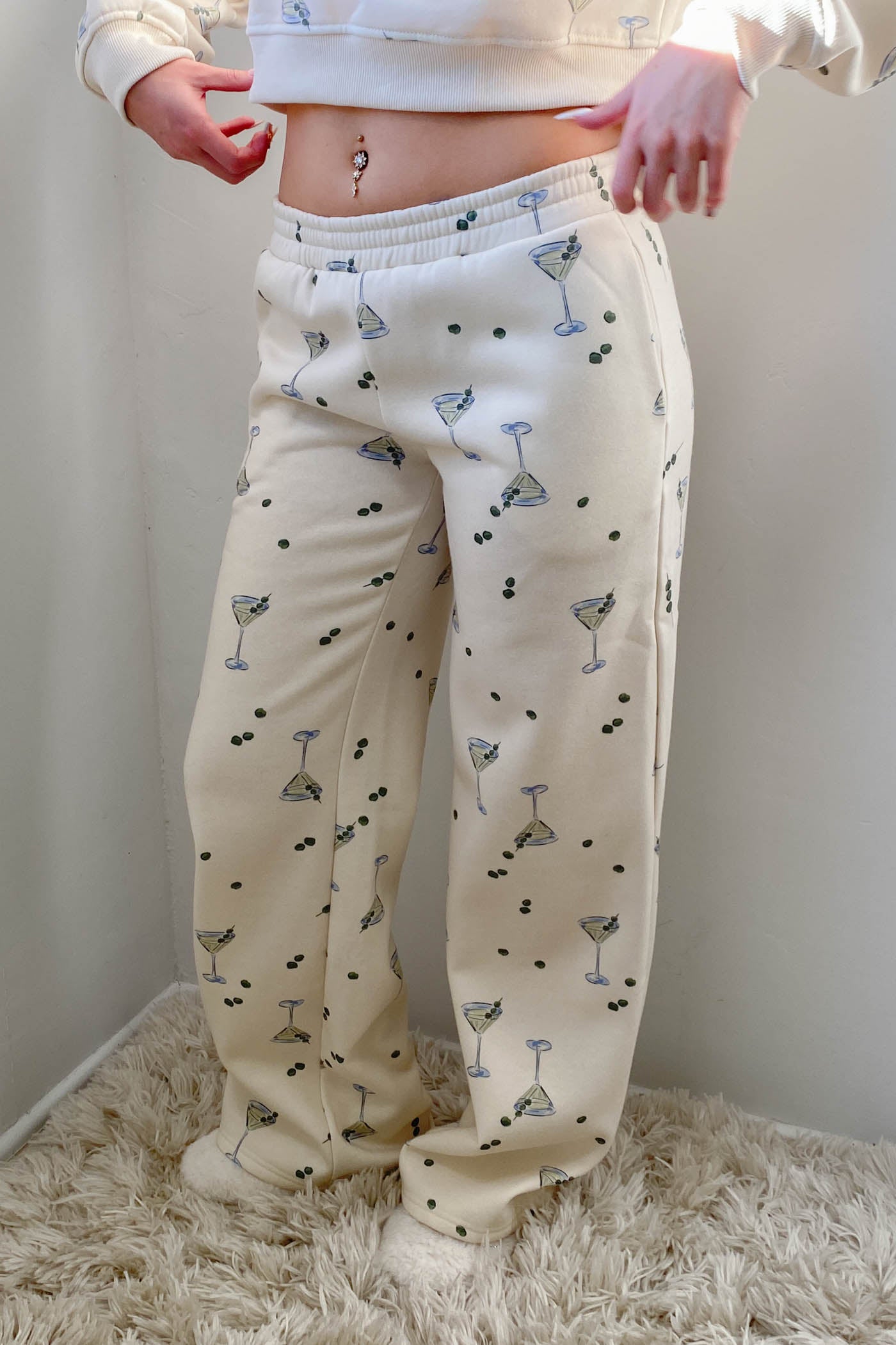 Person wearing cream-colored pajama pants with pattern, standing on a fluffy rug.