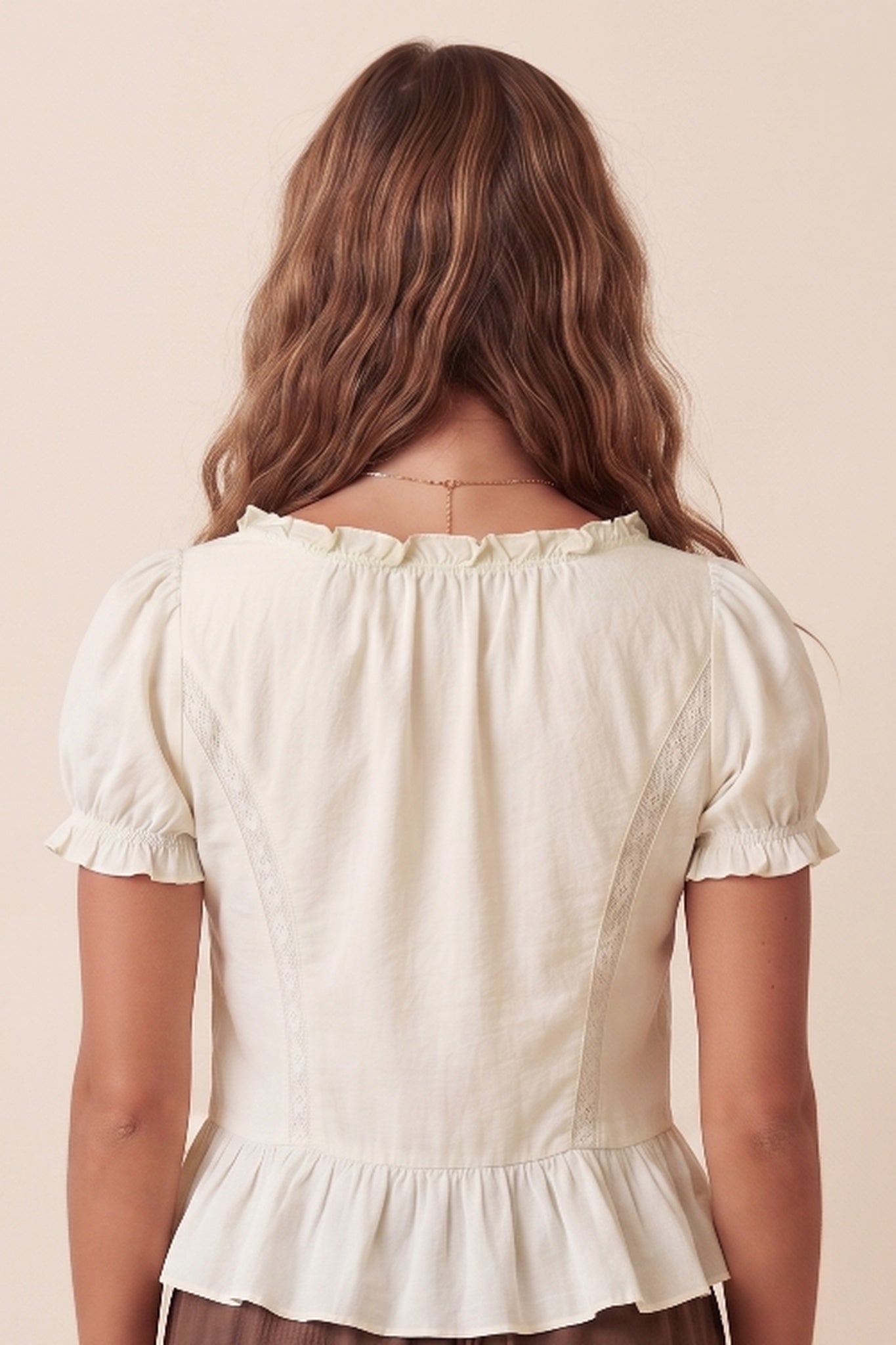 Back view of a woman wearing a cream-colored short-sleeve blouse with ruffled trim and a peplum hem, set against a solid beige background.