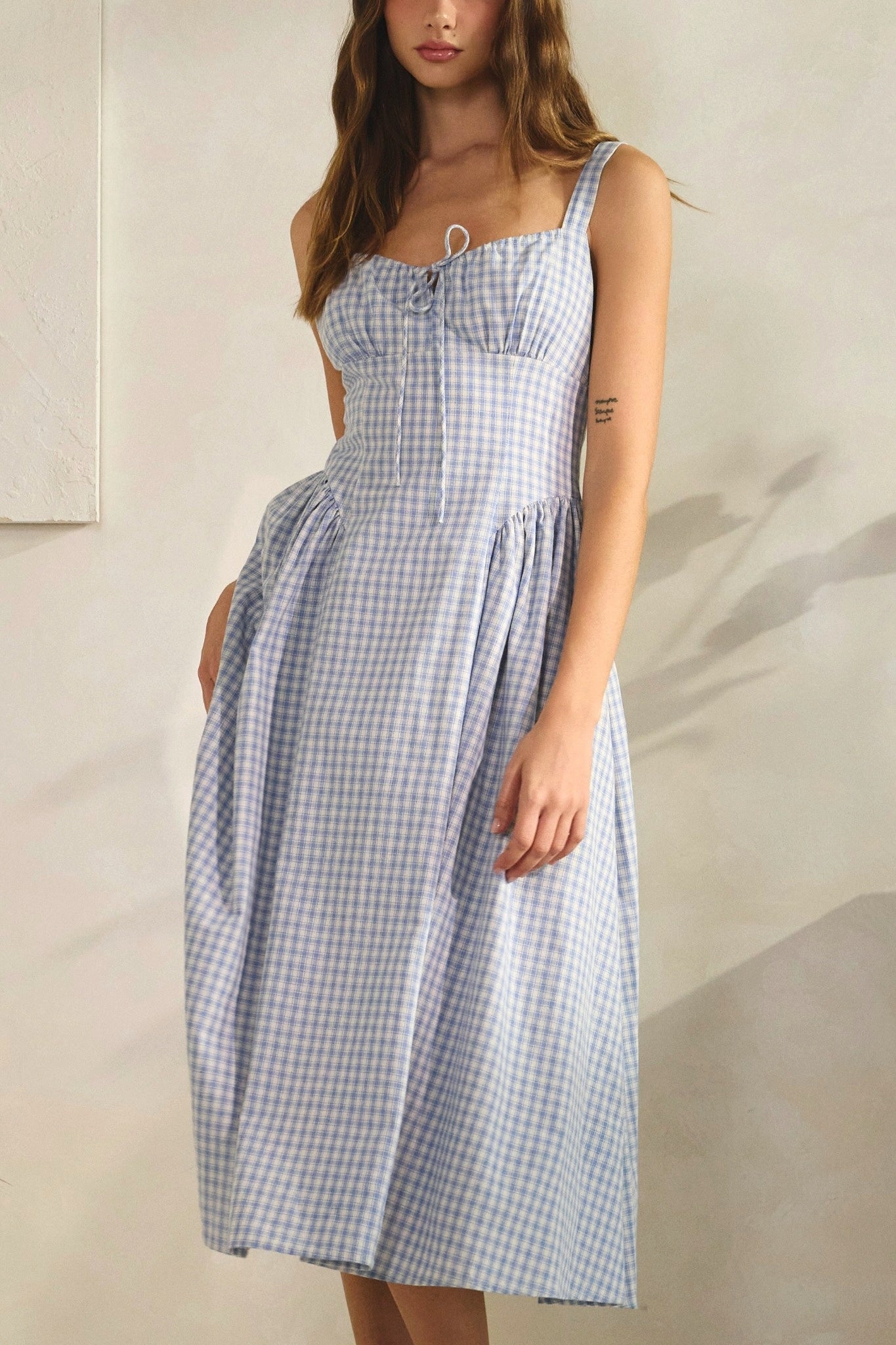 Woman wearing a blue and white checkered dress against a neutral background