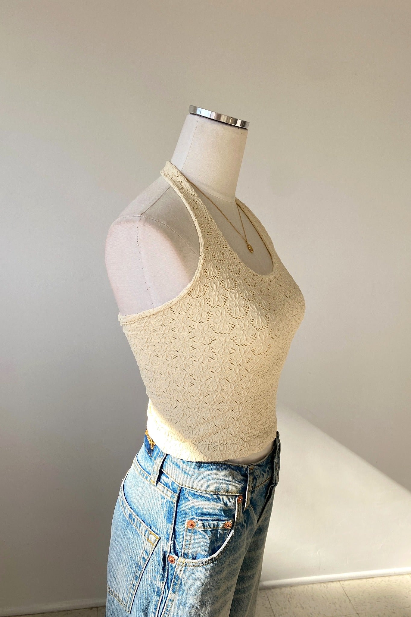Mannequin wearing a beige lace top and blue jeans against a plain background