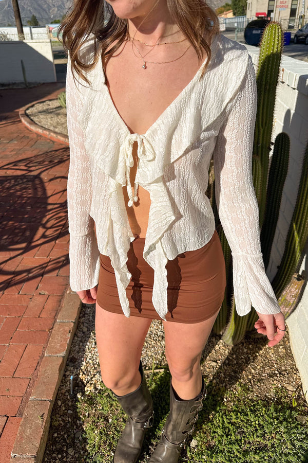 Person wearing a white blouse and brown shorts standing outdoors with a cactus in the background.