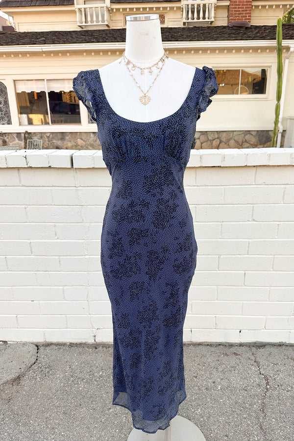 Navy blue lace dress on a mannequin against a white brick wall.