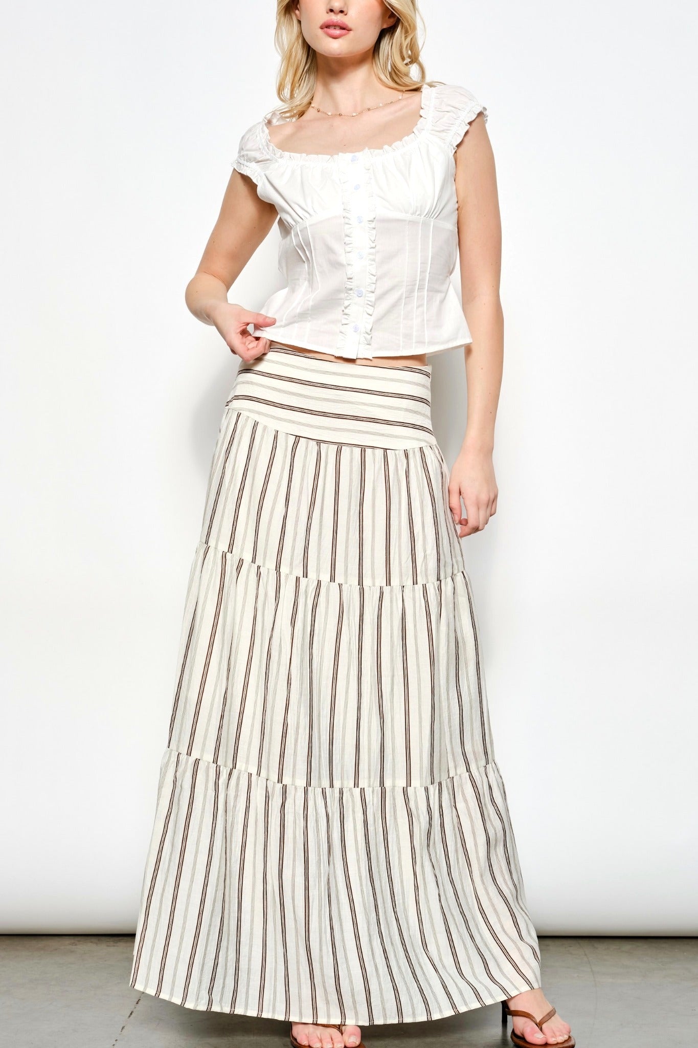 Woman wearing a white top and striped skirt on a plain background