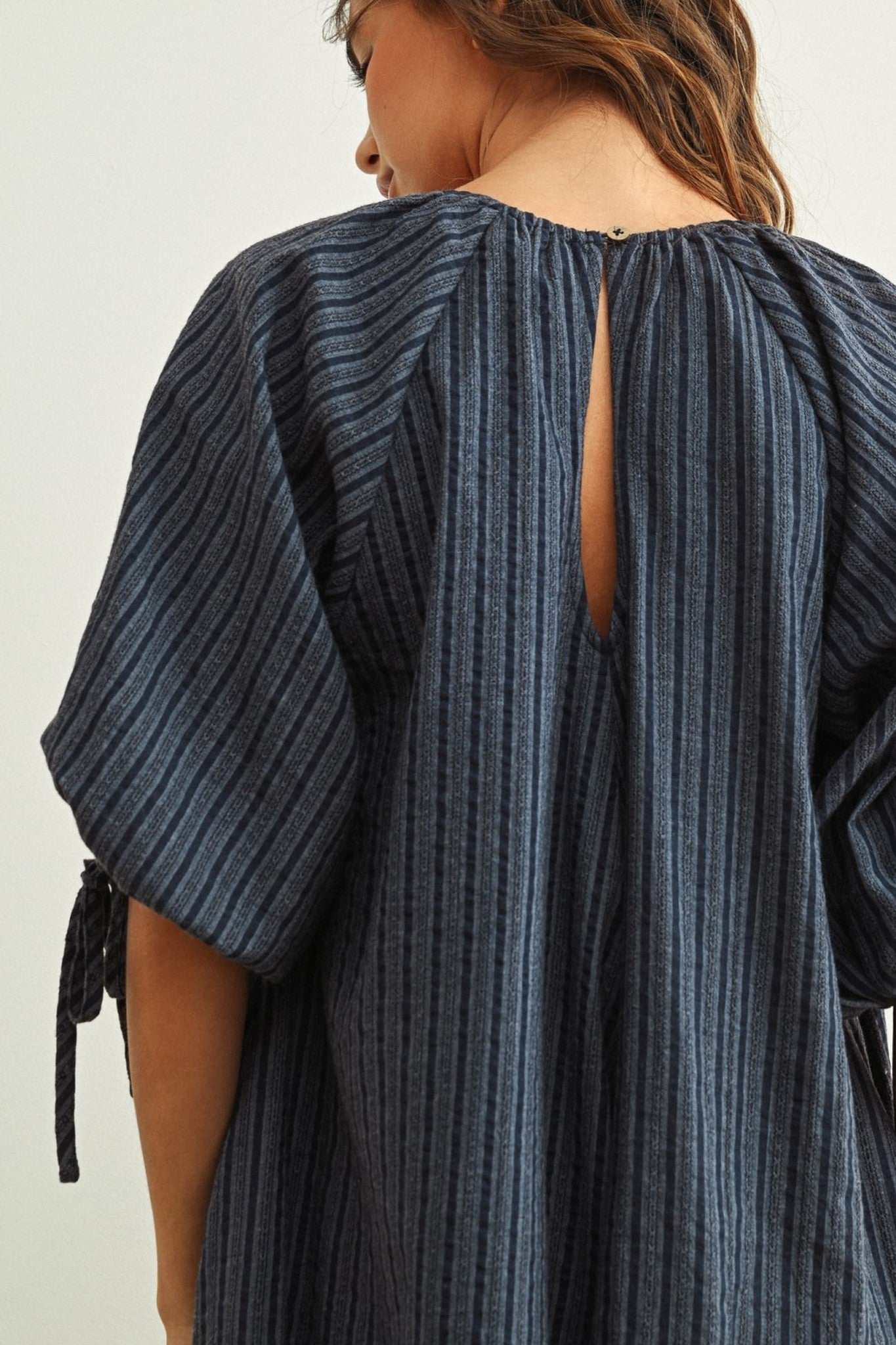 Blue striped dress with open back worn by a person on a white background