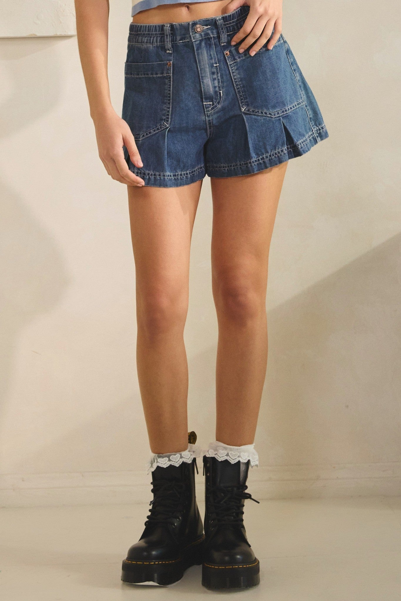 Person wearing a denim skirt and black boots on a neutral background