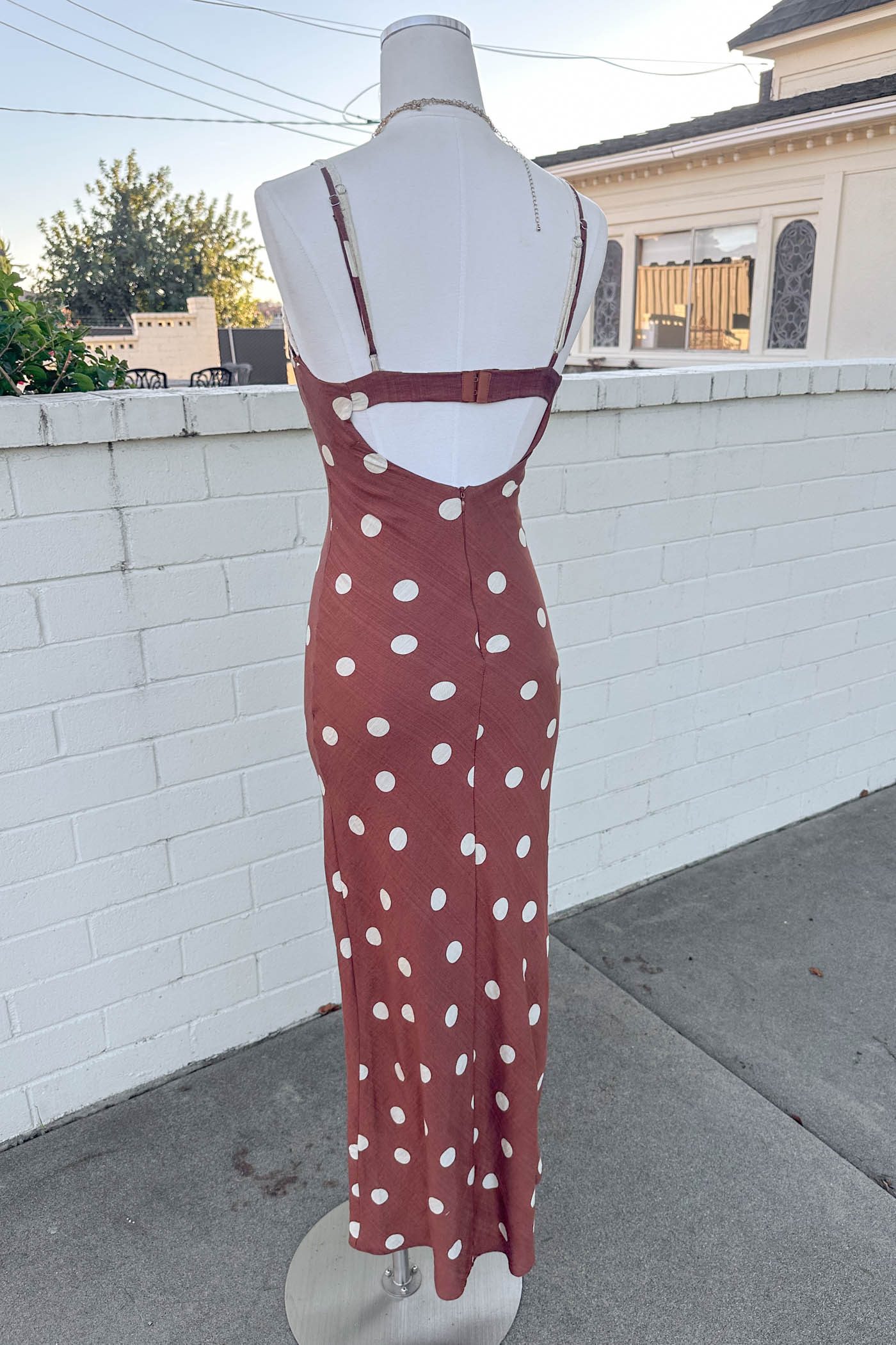 Mannequin wearing a Brown Polka Dotted Maxi Dress standing in front of a brick wall. 