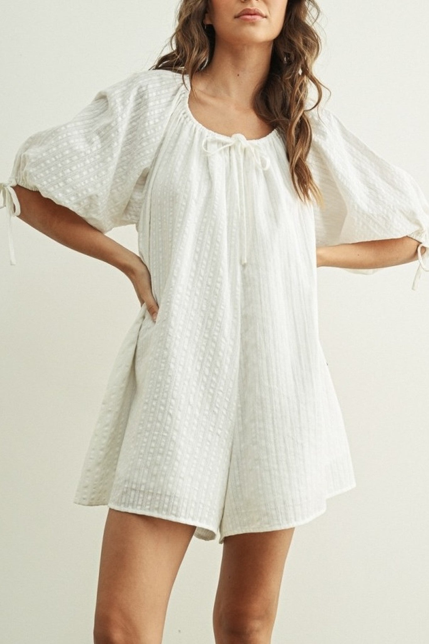 Woman wearing a white dress with a textured pattern on a plain background