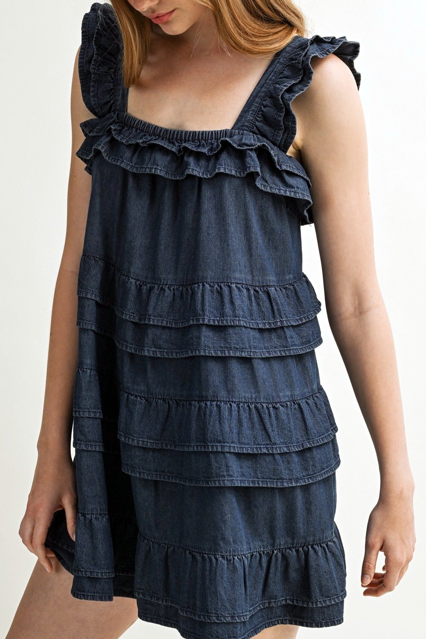 Woman wearing a blue denim dress with ruffled details on a plain background