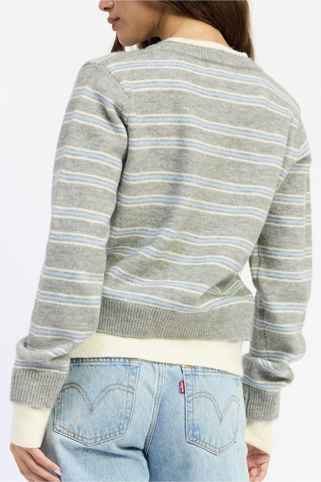 A woman shown from the back wearing a gray knit sweater with thin light blue and white horizontal stripes, paired with light blue jeans.
