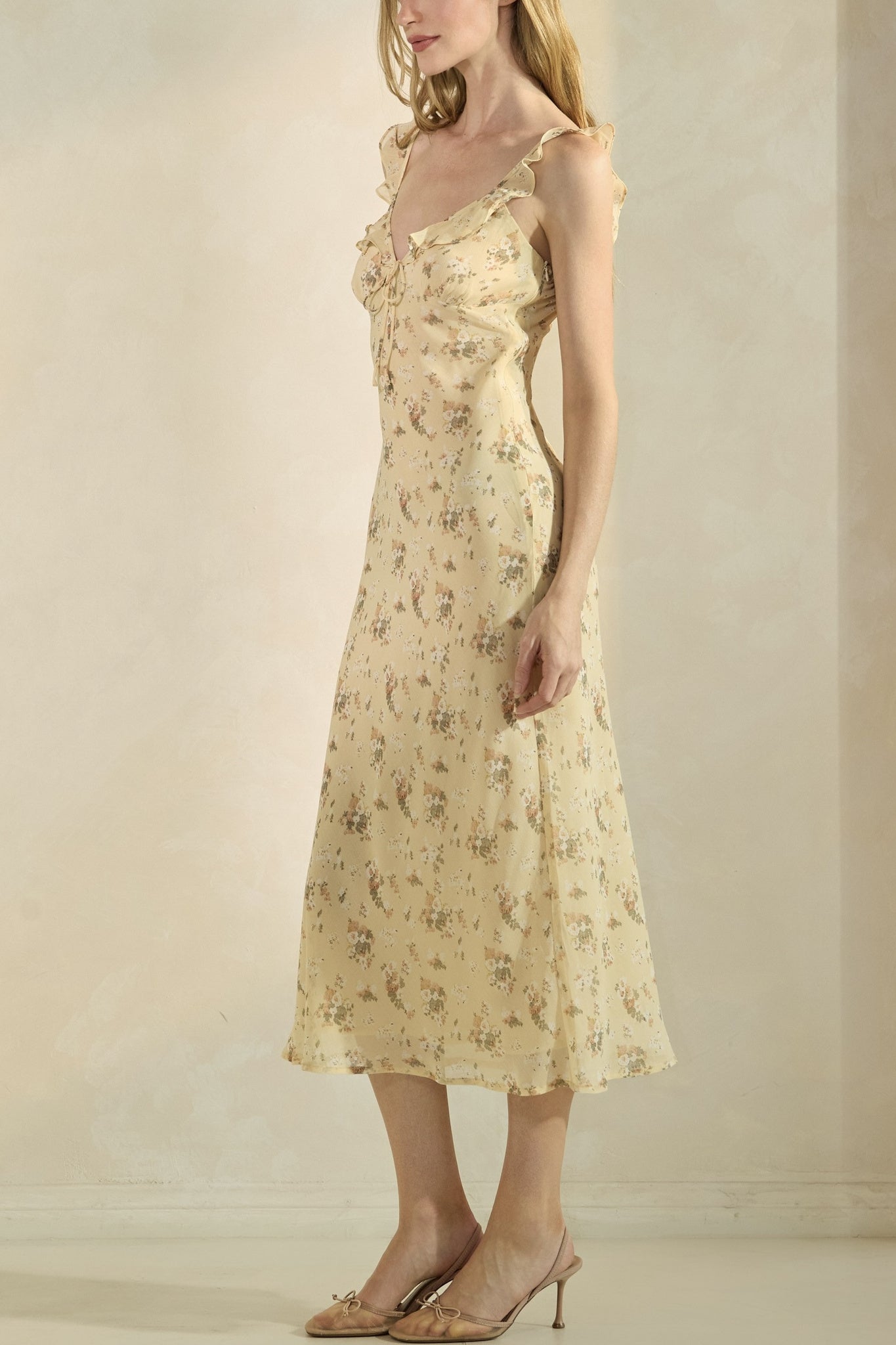 Woman wearing a yellow floral dress against a plain background