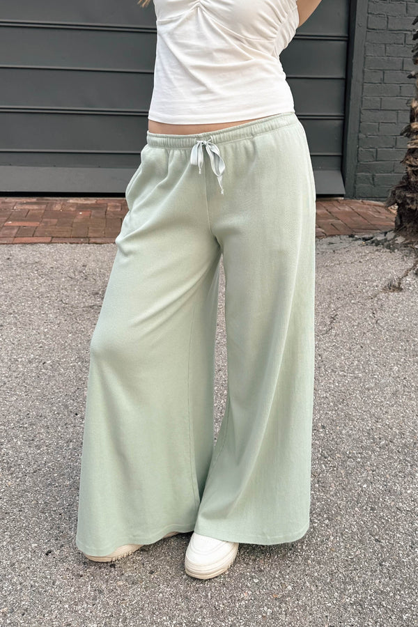 Person wearing light green wide-leg pants and a white top outdoors.