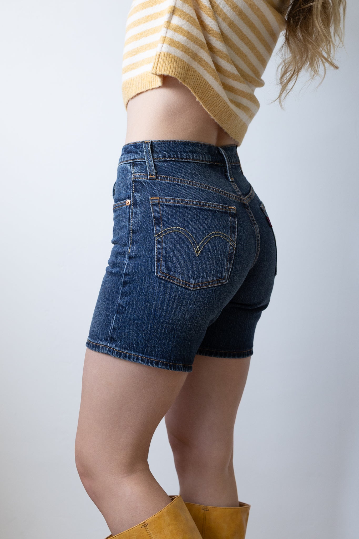 Person wearing blue denim shorts and yellow striped sweater on a plain background