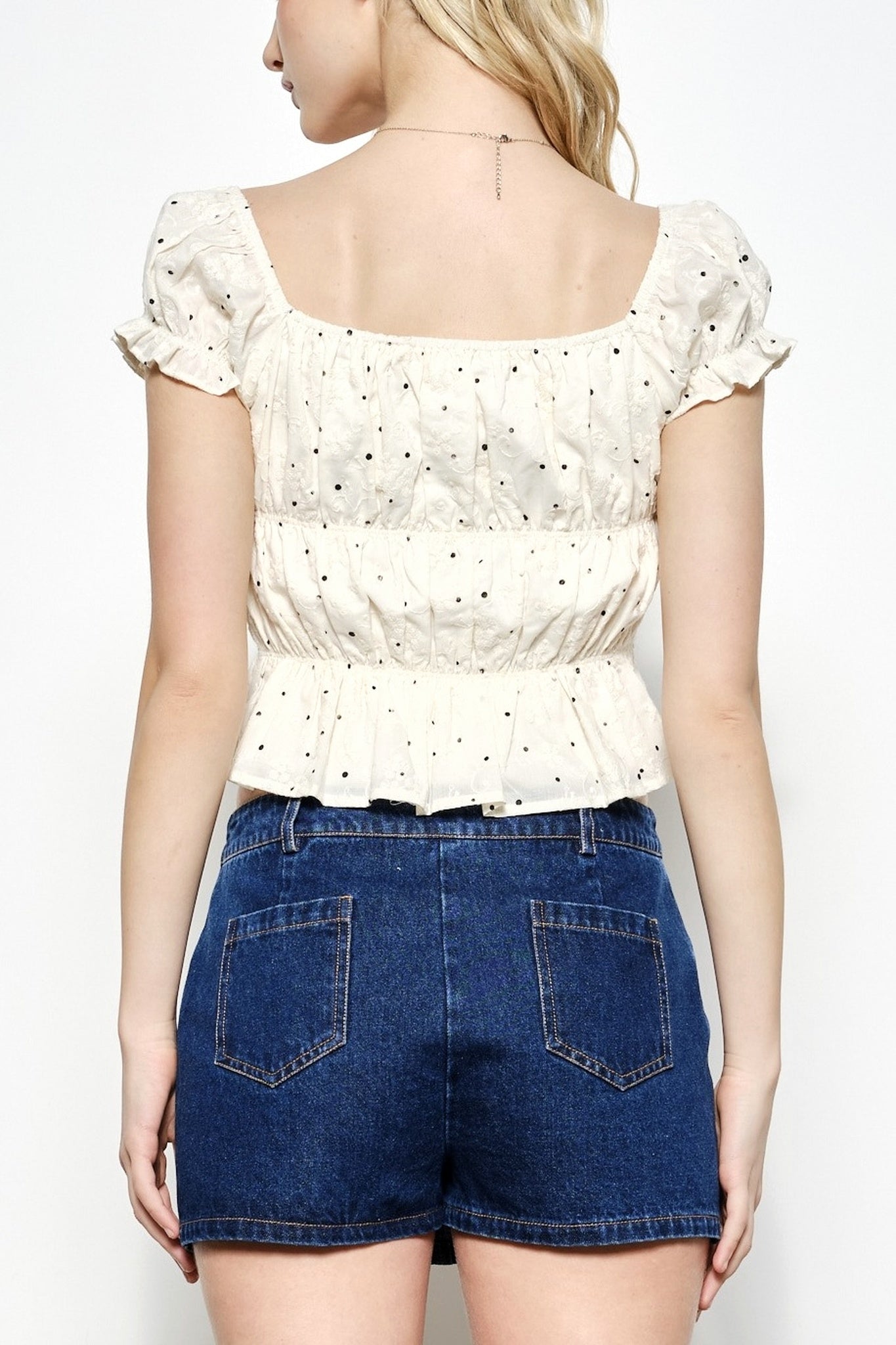 Person wearing a white blouse with ruffled sleeves and blue denim shorts on a plain background