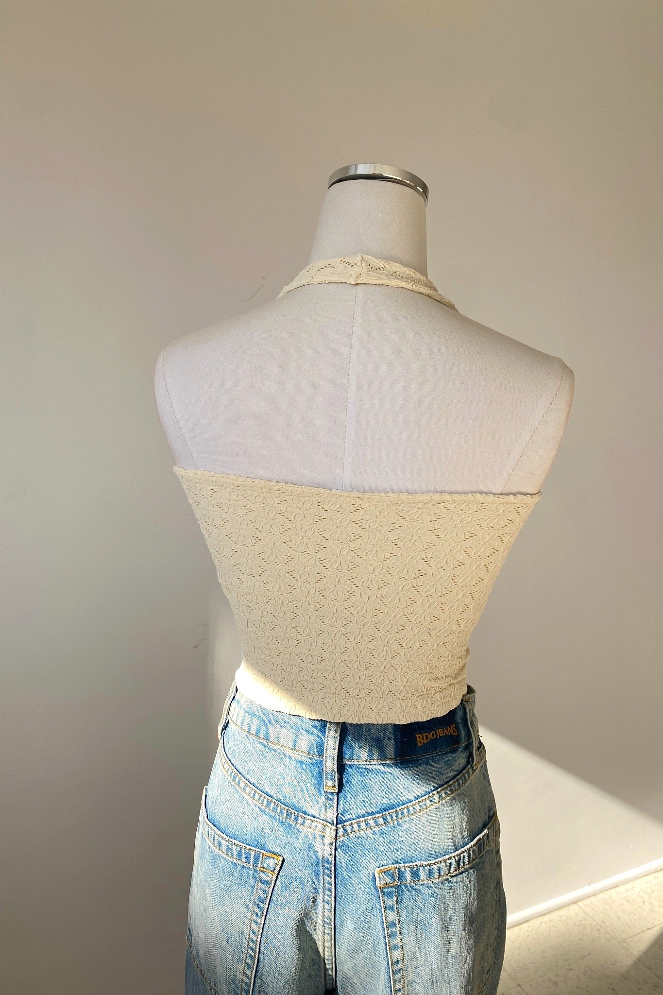Mannequin wearing a beige textured top and blue jeans against a plain background