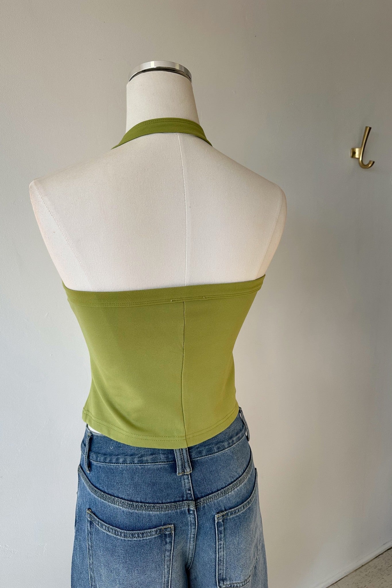 Green halter top on a mannequin with blue jeans against a plain background