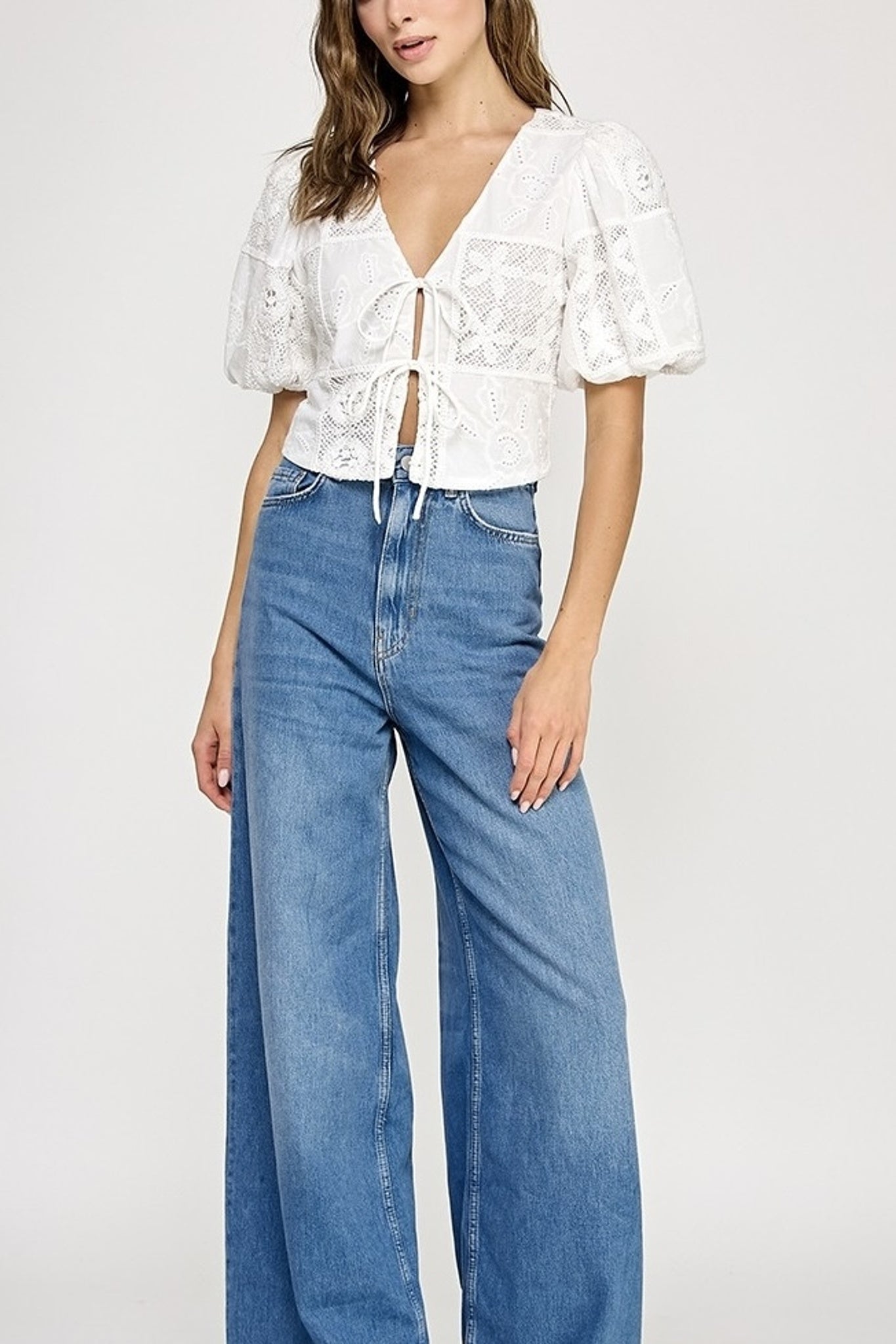 Woman wearing a white lace top and blue jeans on a white background