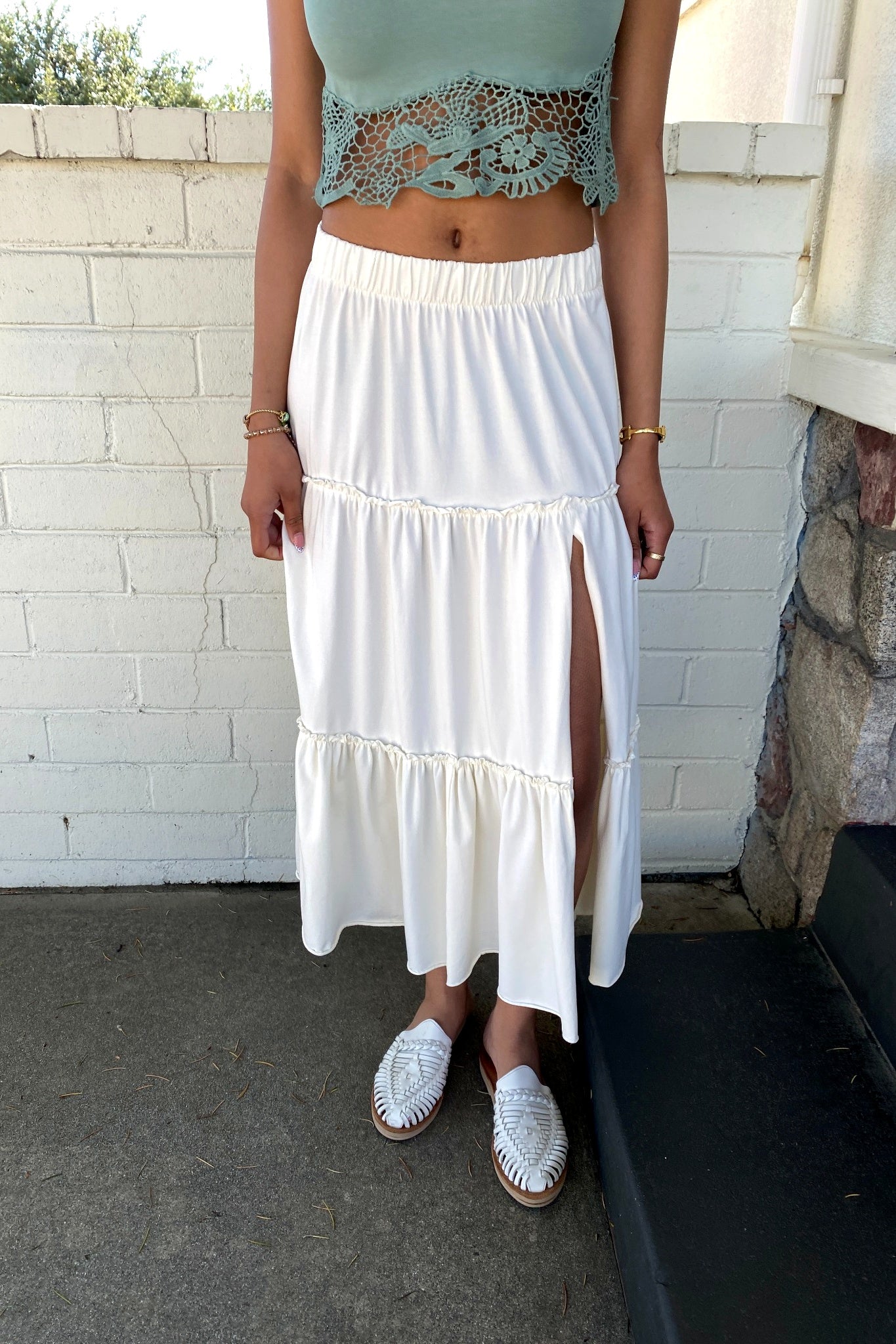 Person wearing a light blue top and white skirt with a stone wall background