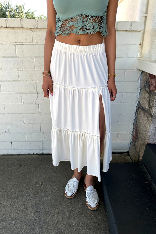 Person wearing a light blue top and white skirt with a stone wall background