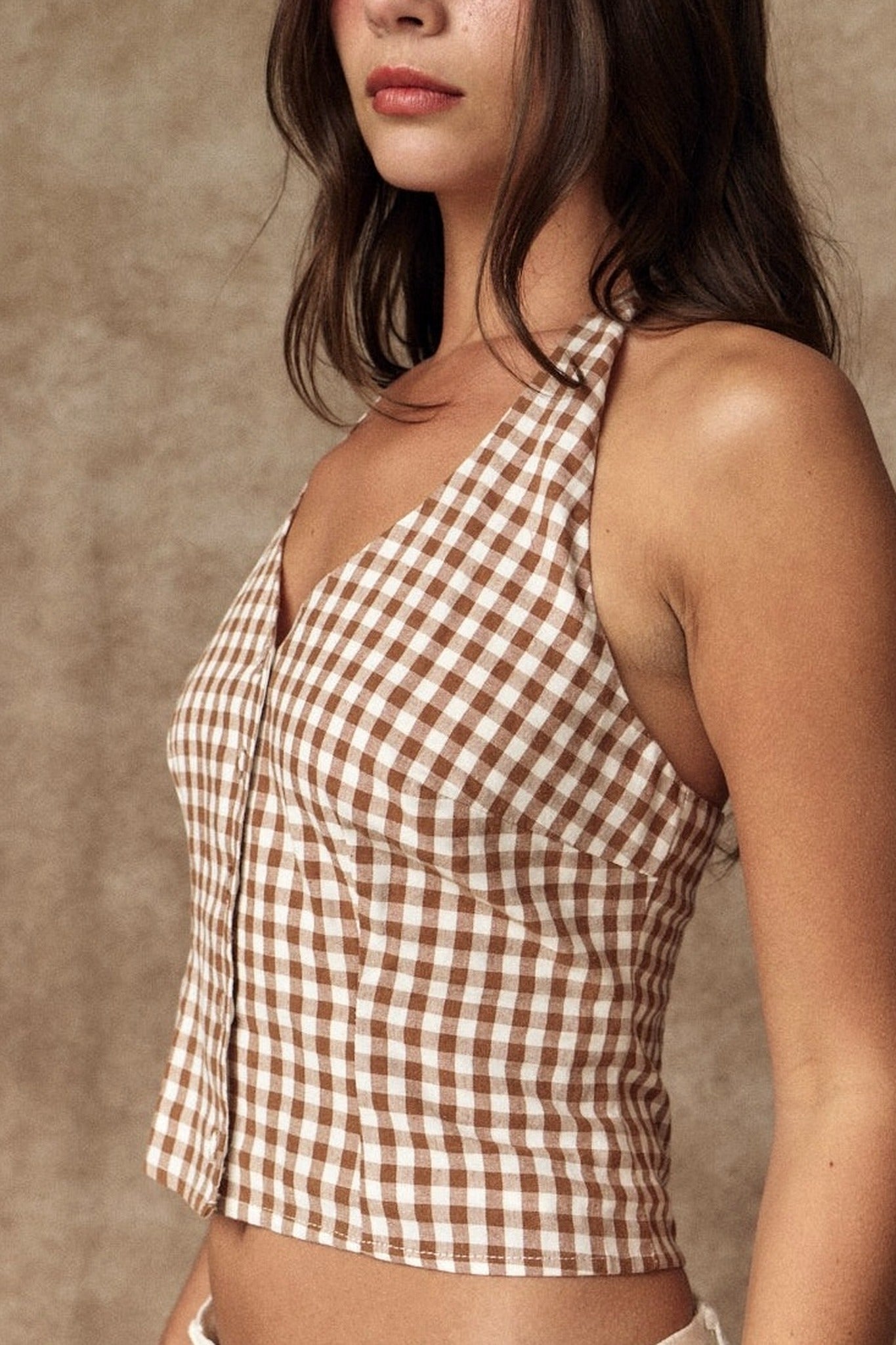 Woman wearing a brown and white checkered halter top against a beige background
