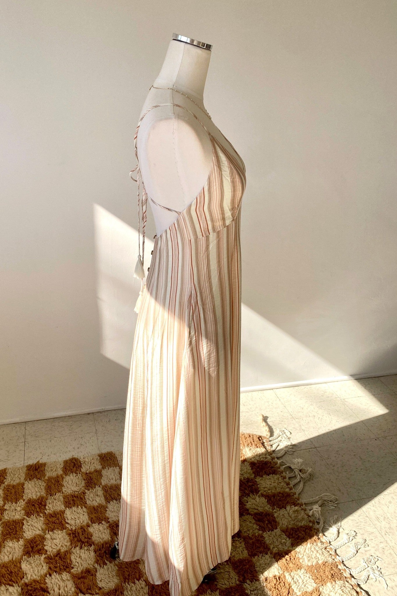 Mannequin wearing a beige and white striped dress on a checkered floor.