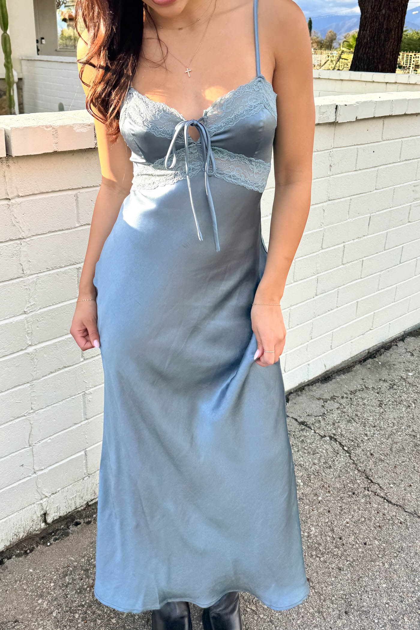 Woman wearing a light blue dress standing against a white brick wall.