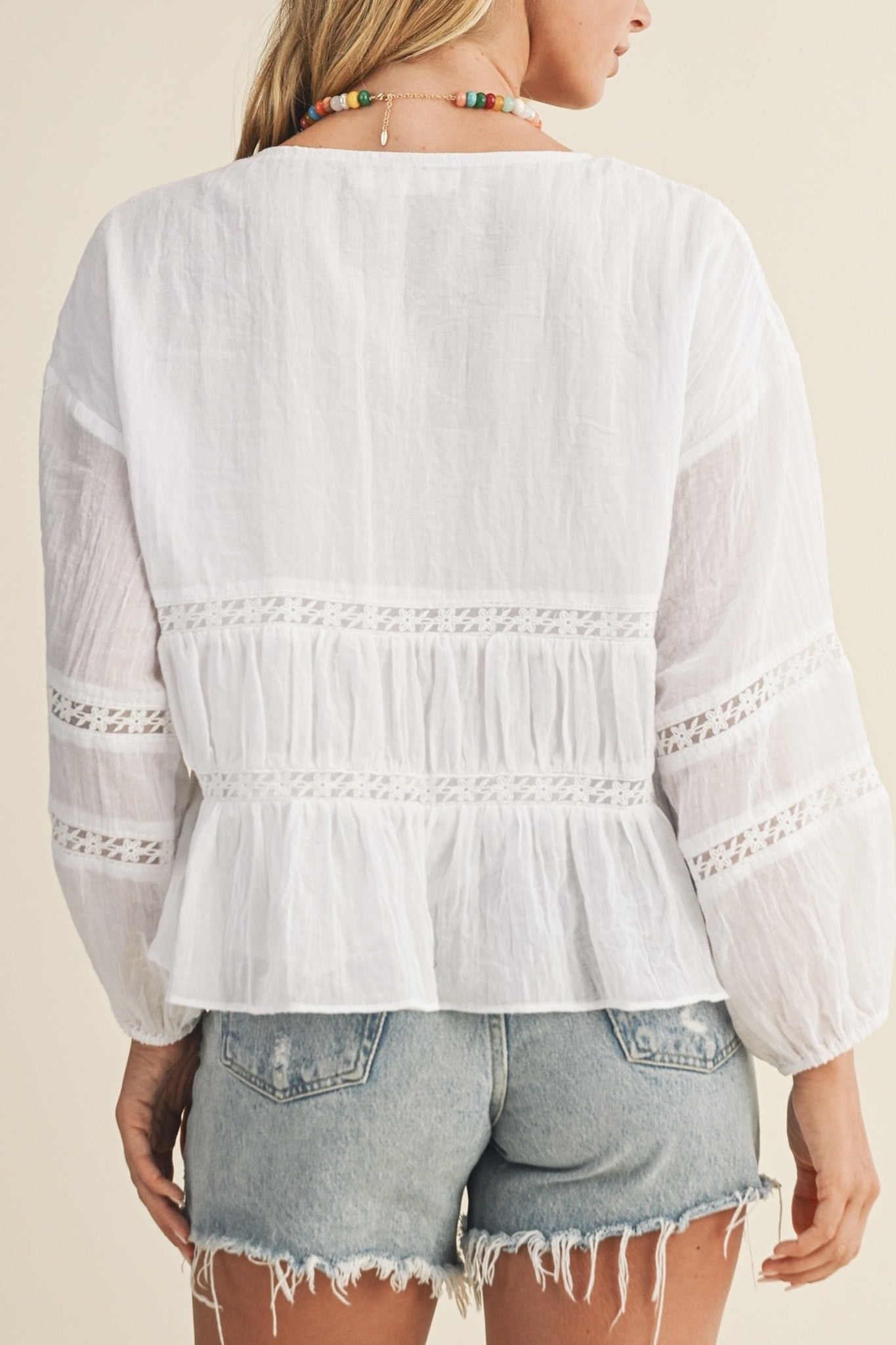 White lace-trimmed blouse worn by a person on a beige background