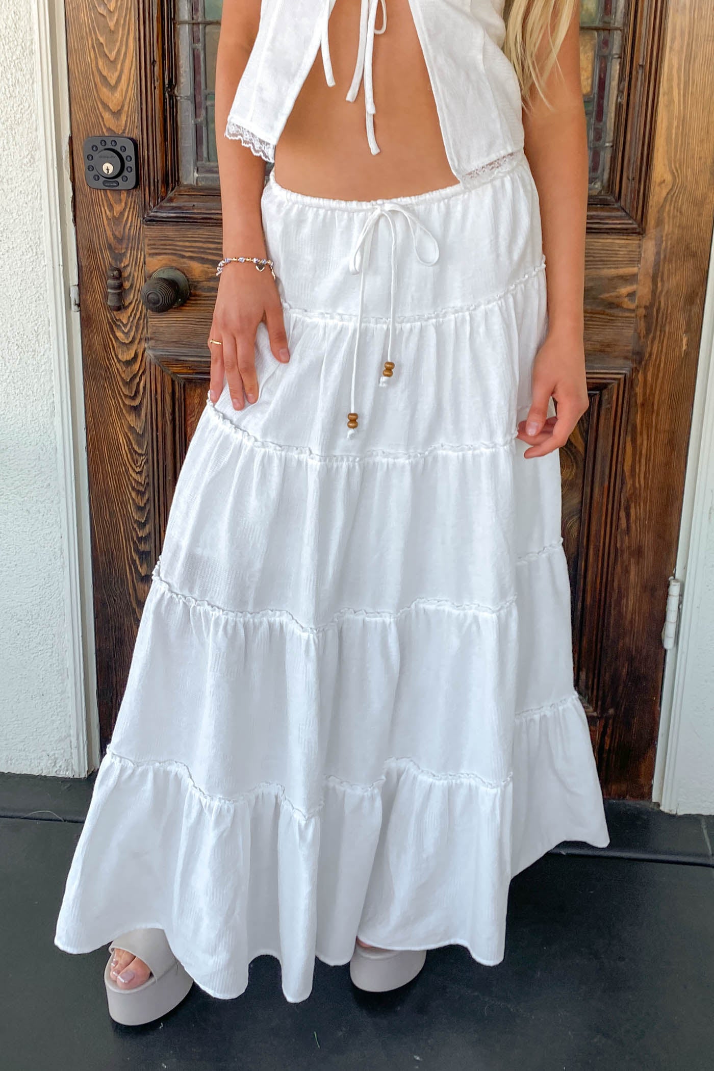 Person wearing a white dress standing in front of a wooden door.