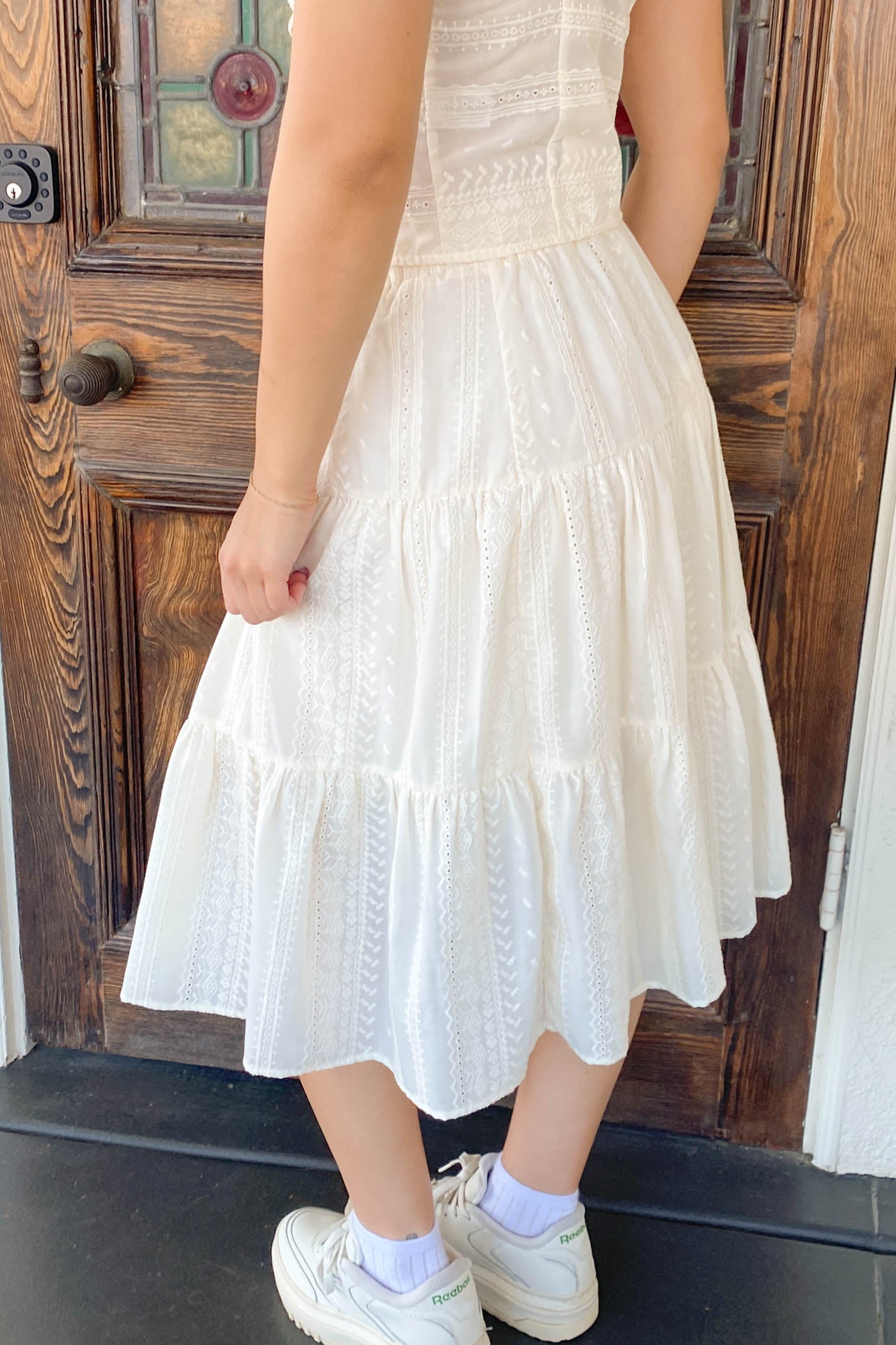 Person wearing a white dress standing in front of a wooden door.