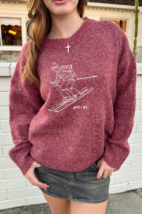 Person wearing a maroon sweater with a graphic design in front of a white brick wall.