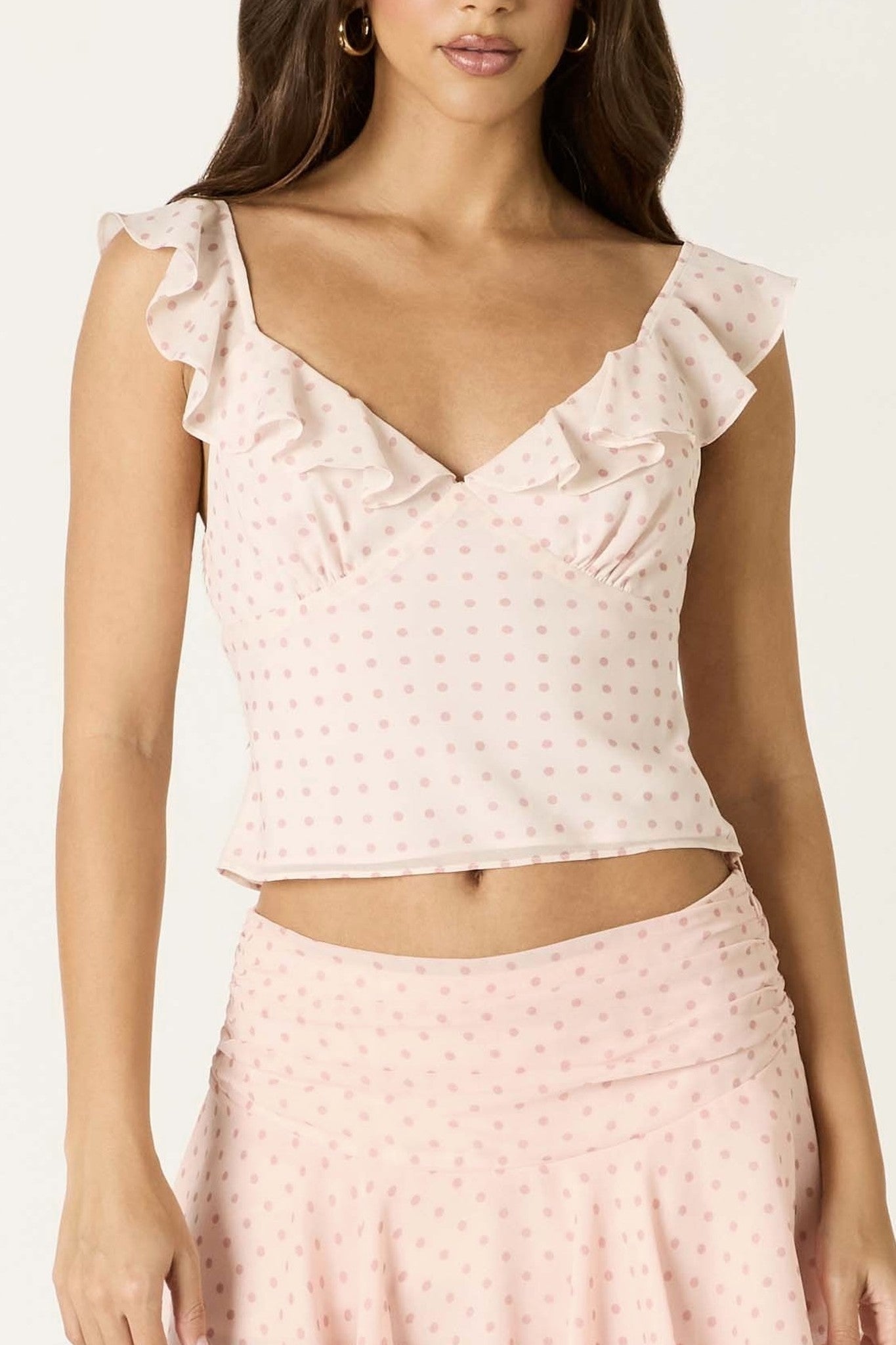 Woman wearing a light pink polka dot top and skirt set on a white background