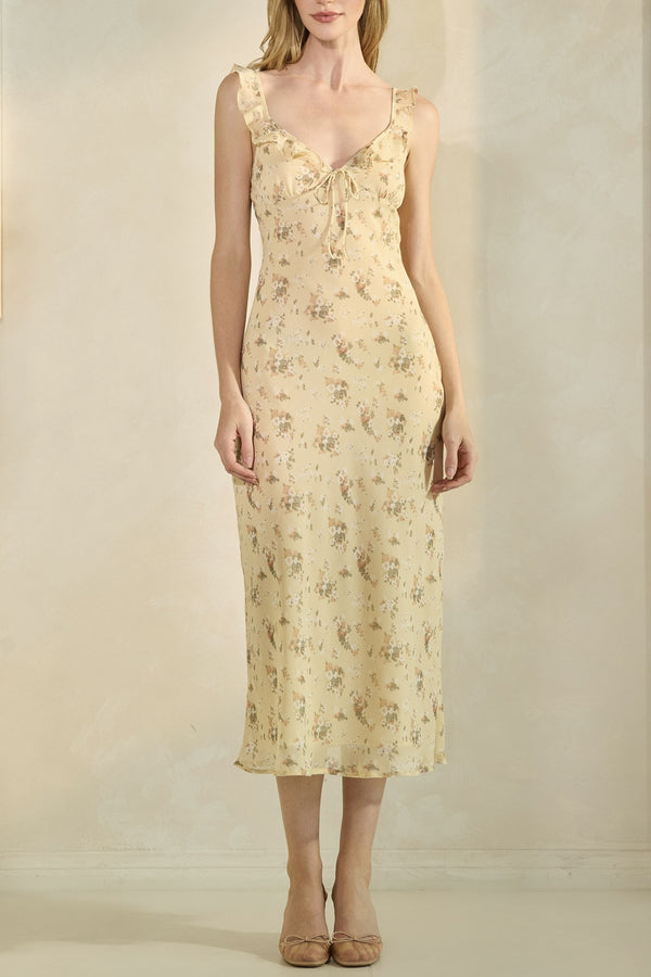 Woman wearing a yellow floral dress against a plain background