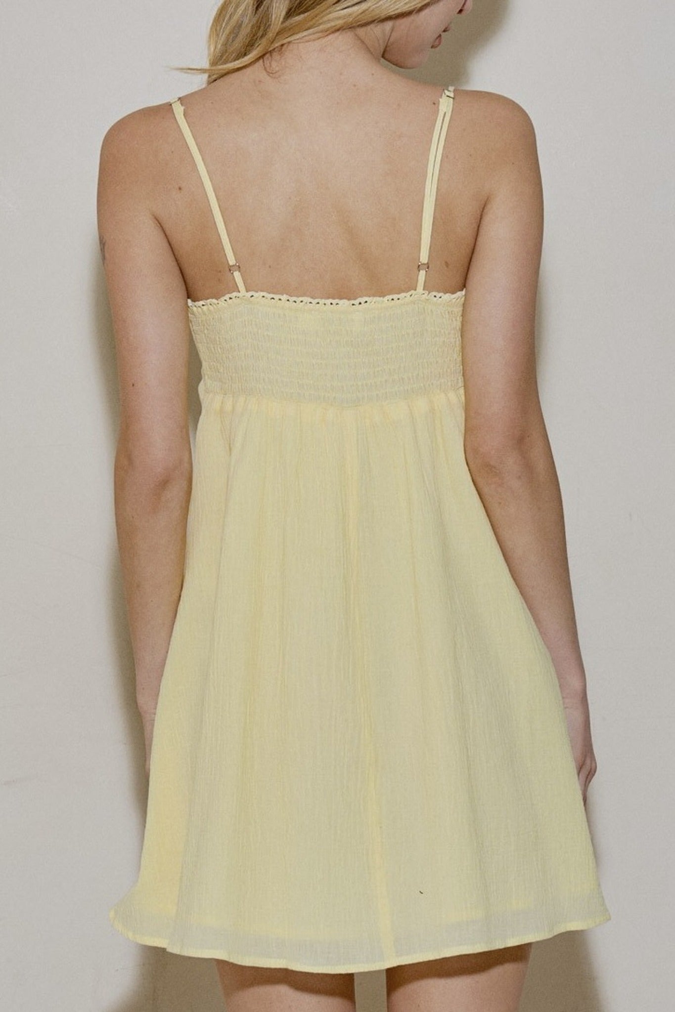 Yellow dress with thin straps worn by a person against a plain background