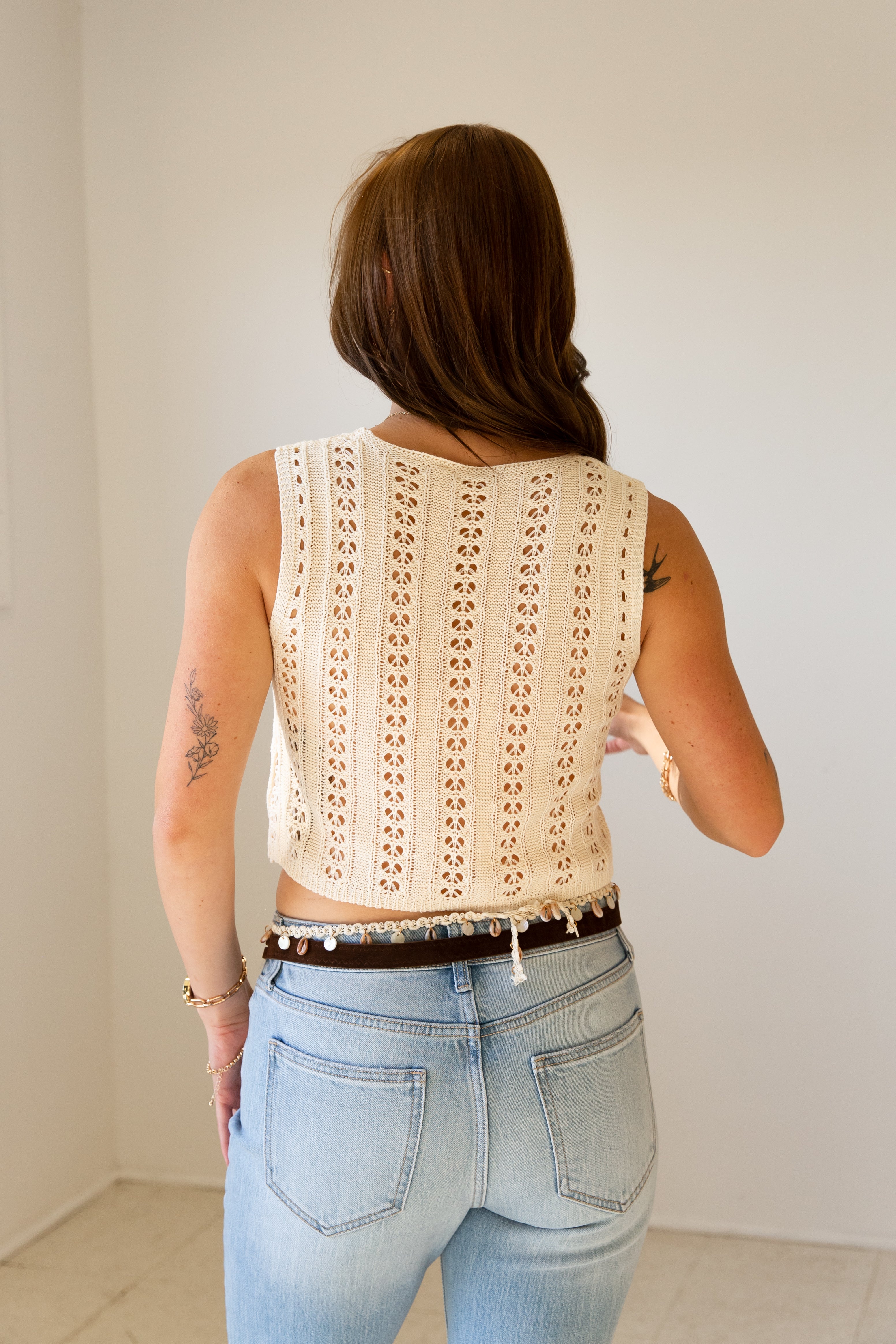 Person wearing a beige crochet top and light blue jeans against a plain background