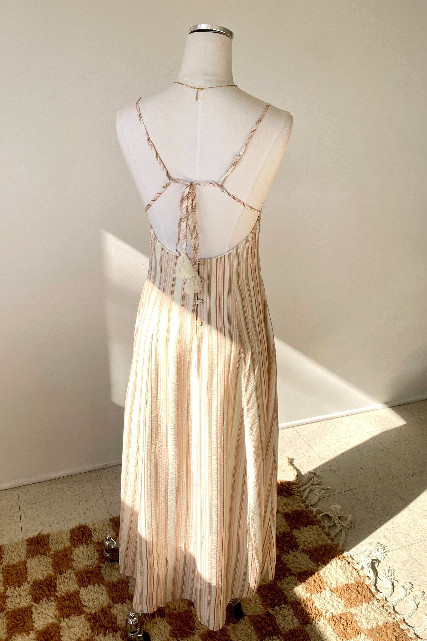 Mannequin wearing a beige dress with geometric cut-out design on a checkered floor.
