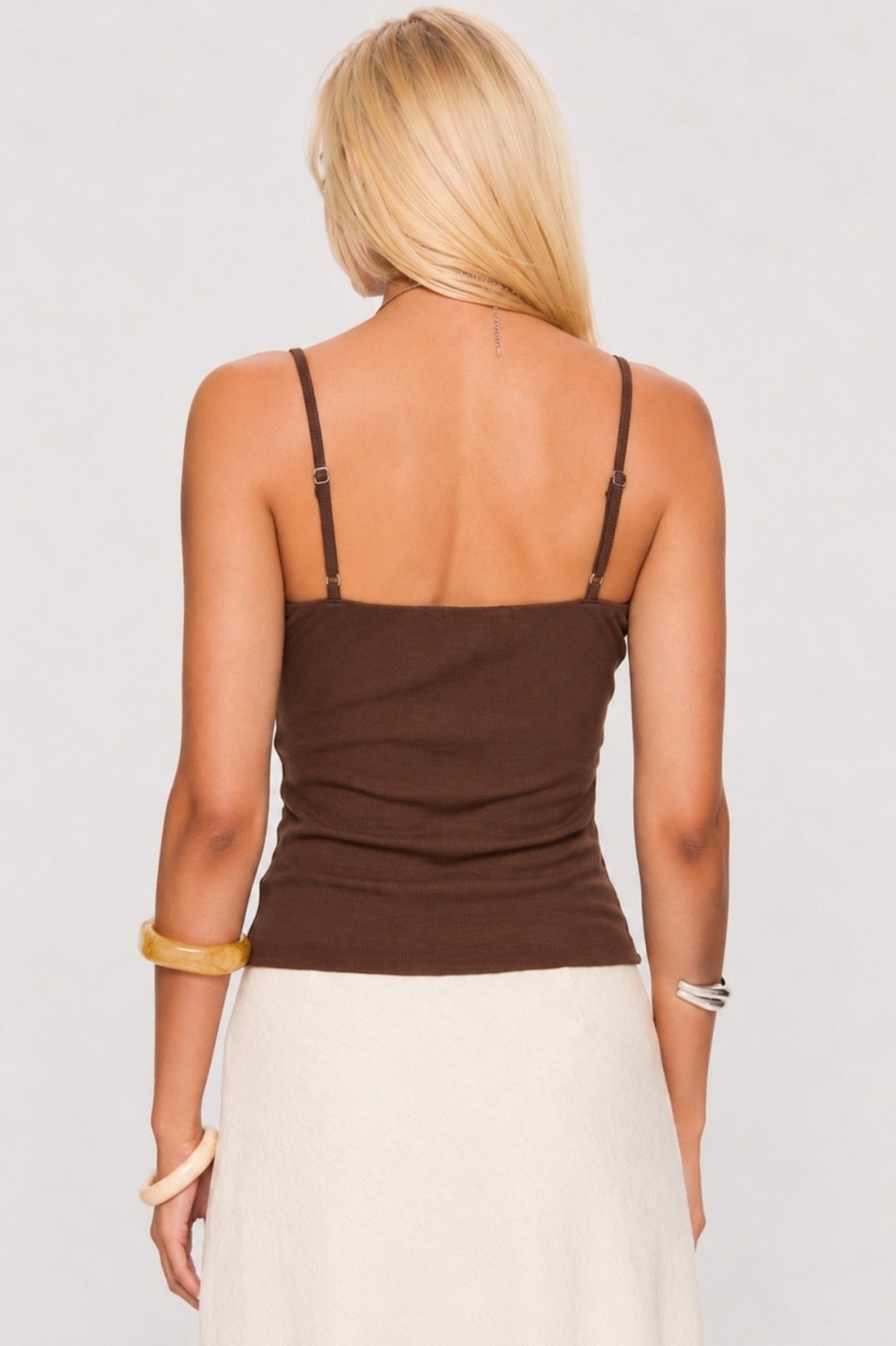 Woman wearing a brown tank top and white pants against a plain background