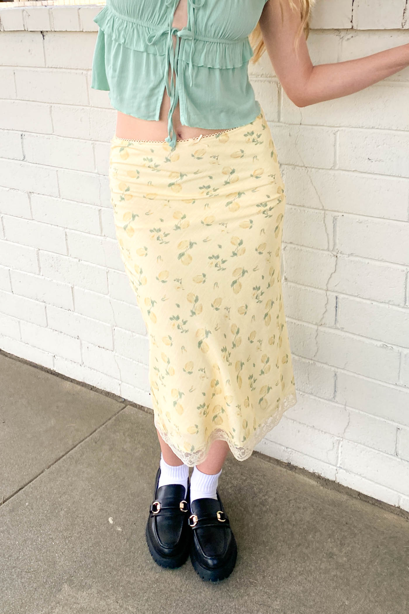 Person wearing a green top and yellow skirt against a white brick wall.