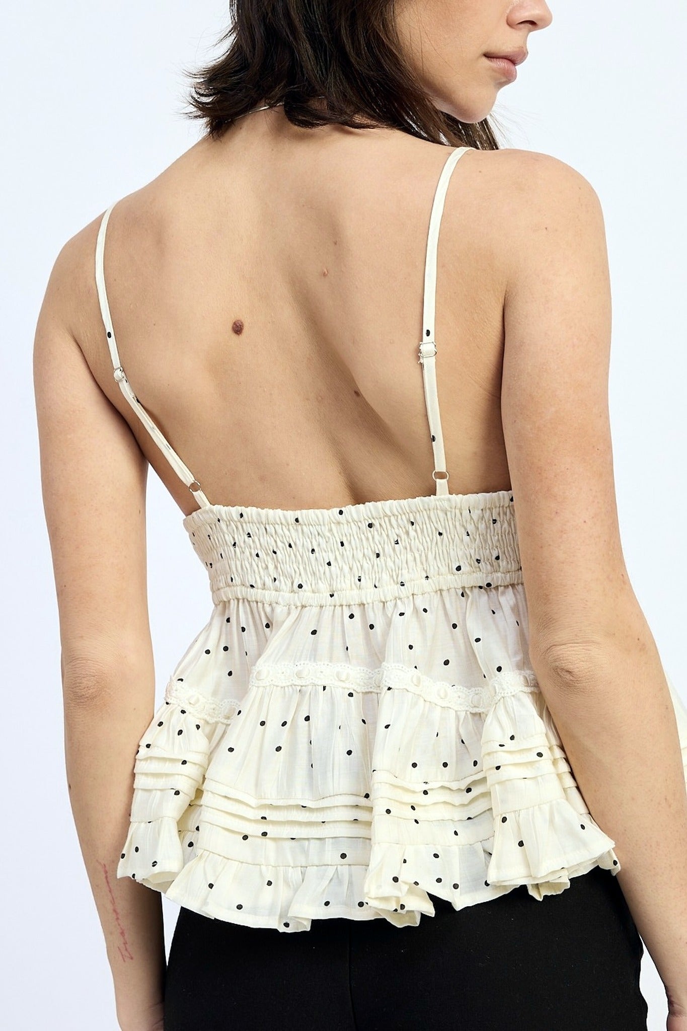 Woman wearing a white peplum top with thin straps on a light gray background