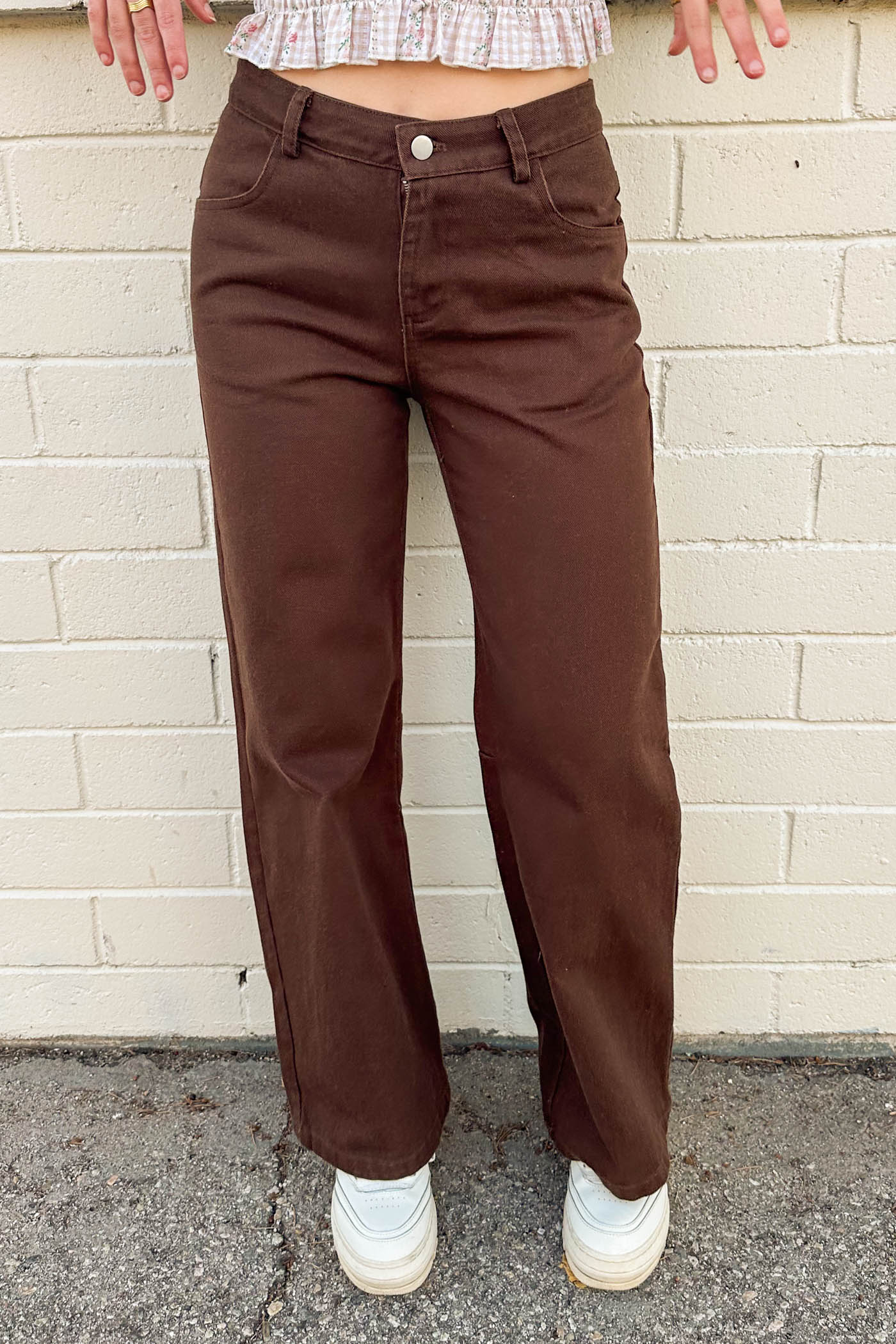 Brown pants worn by a person standing against a beige brick wall.
