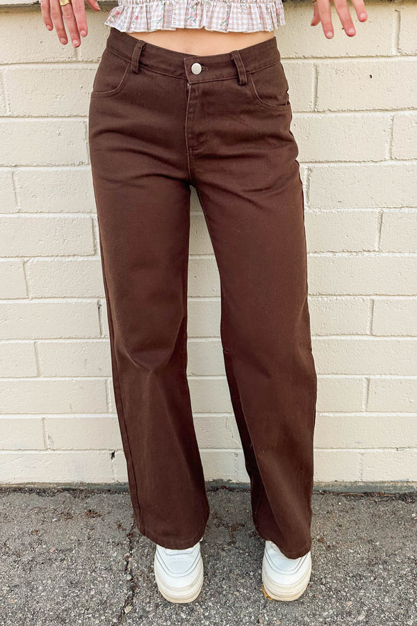 Brown pants worn by a person standing against a beige brick wall.