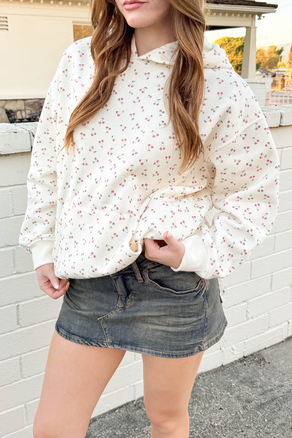 Person wearing a white floral hoodie and denim shorts standing against a white brick wall.