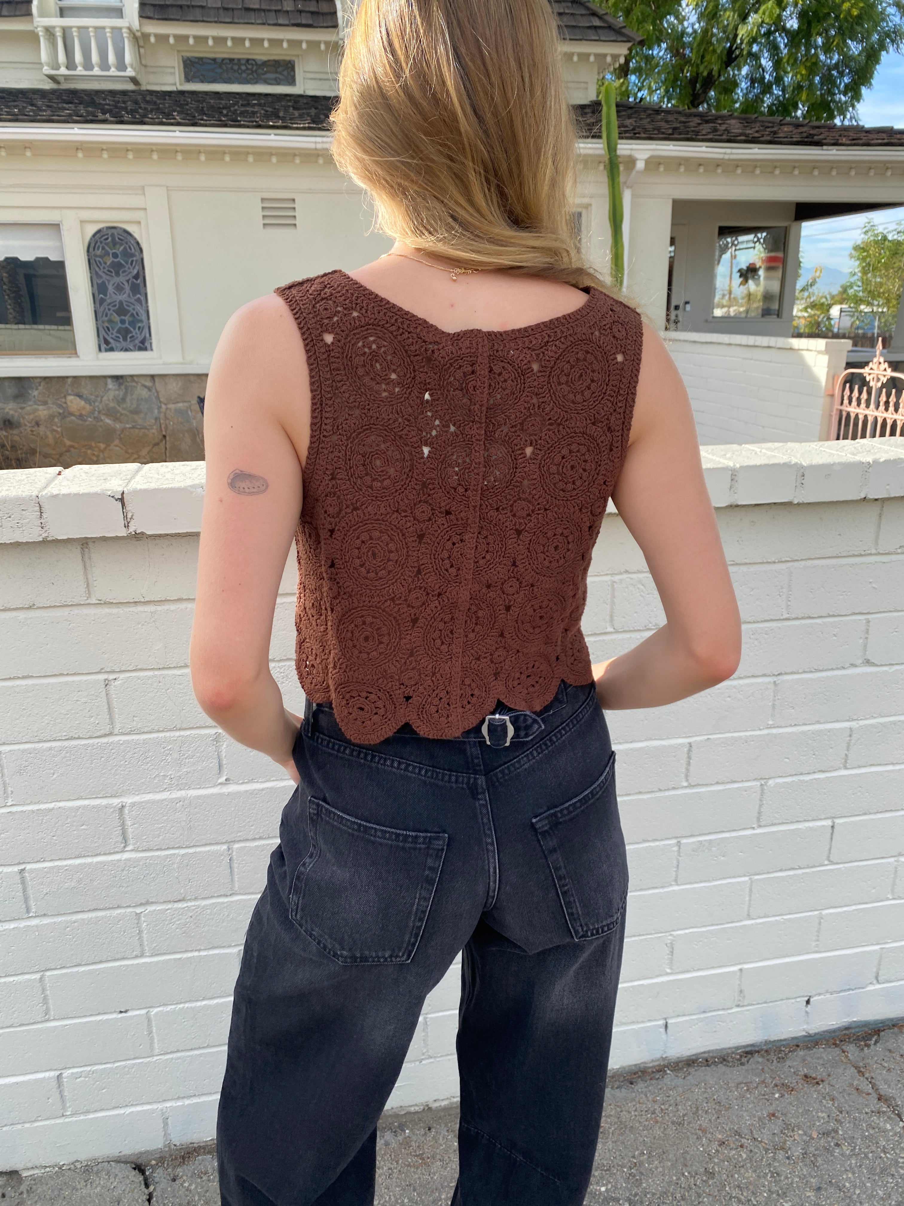 Person wearing a brown sleeveless top and dark pants on a sidewalk.