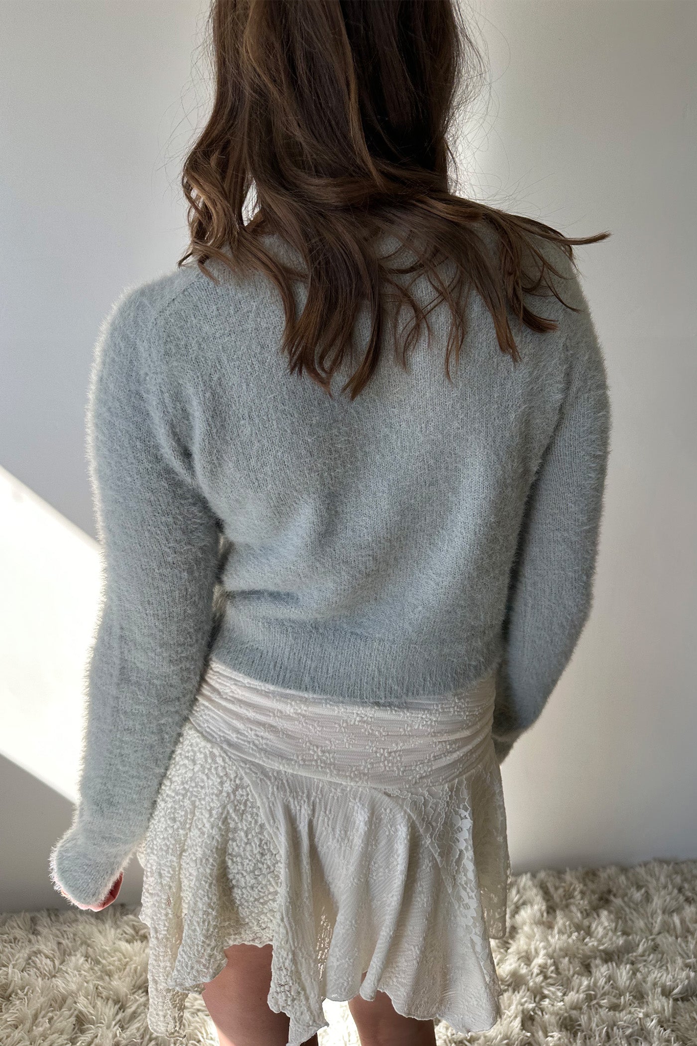 Person wearing a light blue sweater and white lace skirt against a neutral background