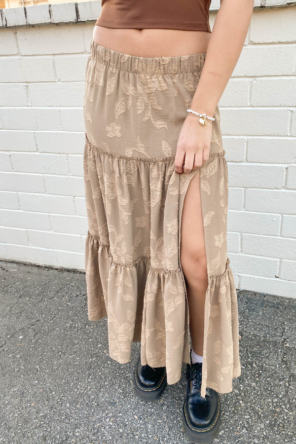 Person wearing a beige tiered skirt with a white brick wall background