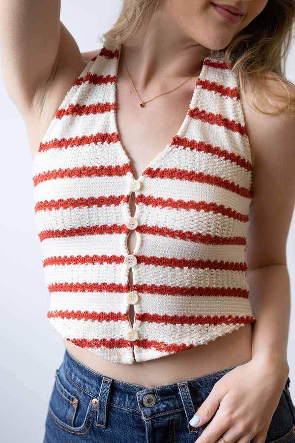 Woman wearing a red and white striped sleeveless top with blue jeans on a light gray background