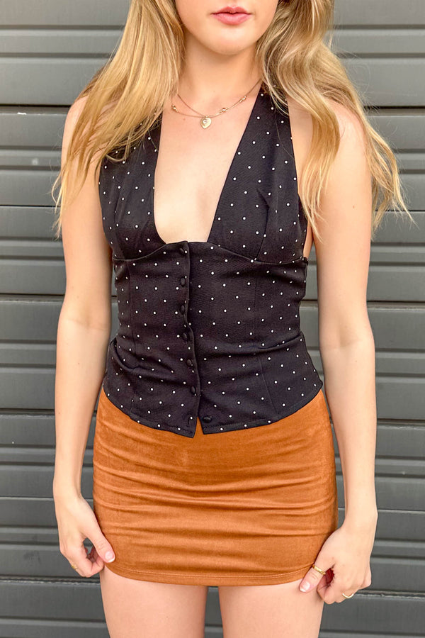 Woman wearing a black polka dot top and brown skirt against a gray background