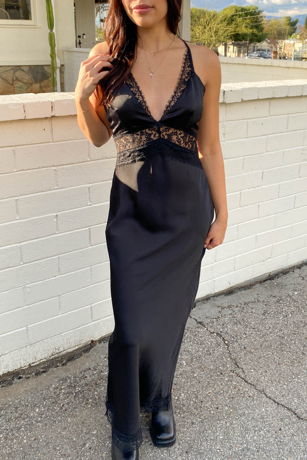 Woman wearing a black evening gown with lace details against a white wall.