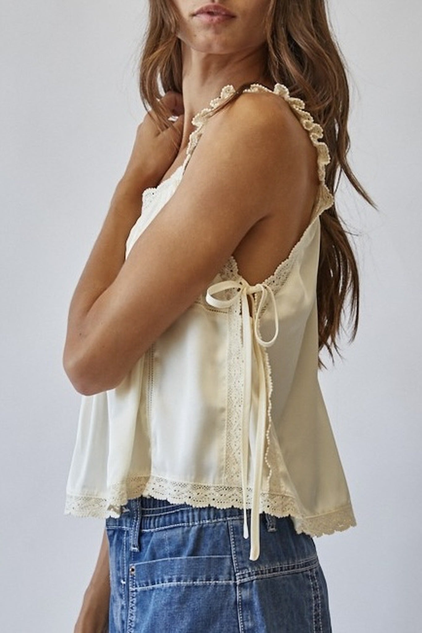 Woman wearing a cream lace top and blue jeans against a white background