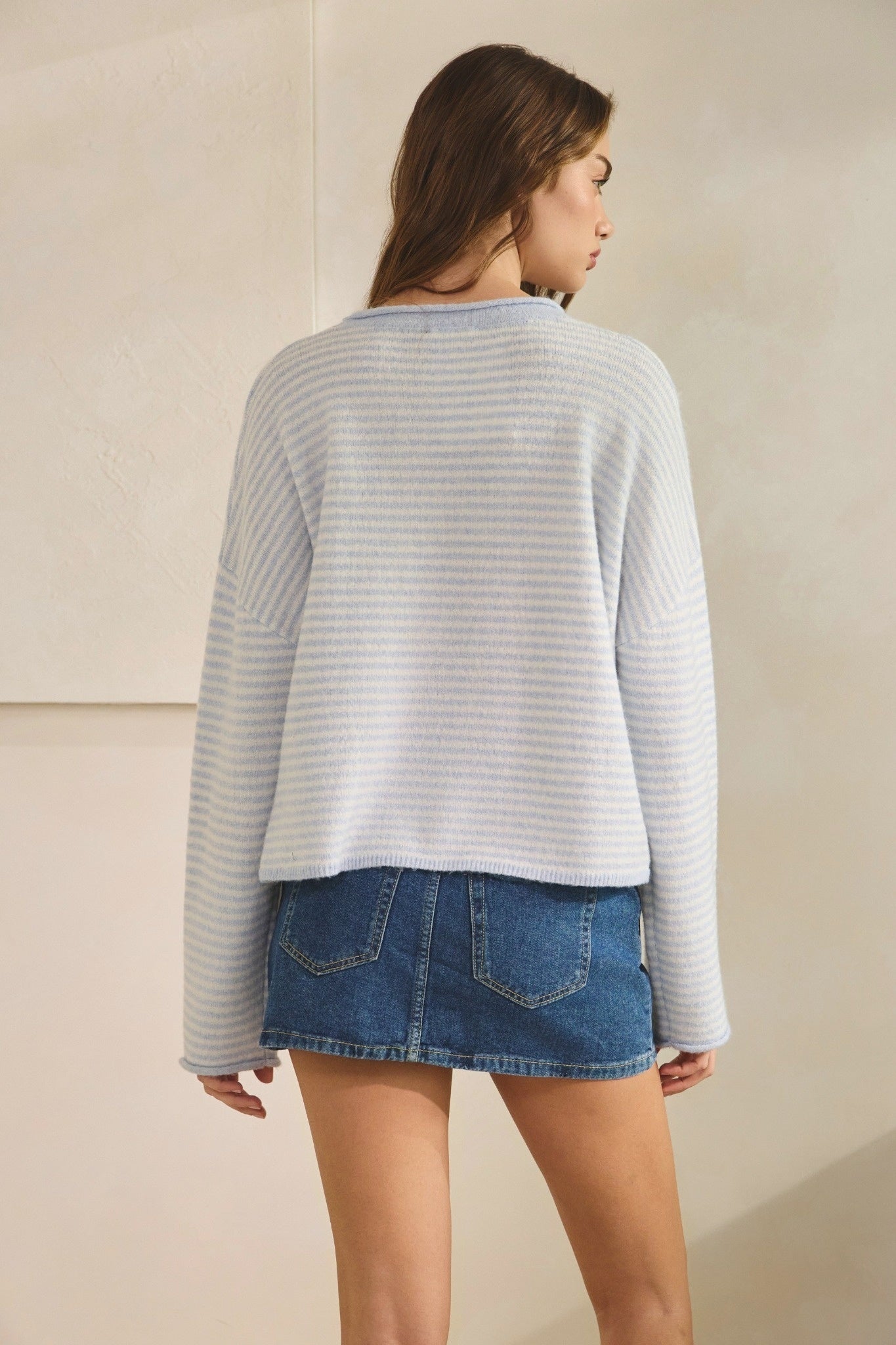 Woman wearing a striped sweater and denim skirt against a beige background